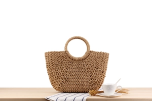 Close-up of semi-circle straw tote bag with round handle on a minimalist wooden table