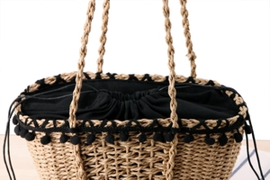 Detail of straw beach bag featuring black pom-poms and drawstring inner lining