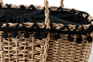 Close-up of paper rope woven beach bag with black pom-pom trim and drawstring lining