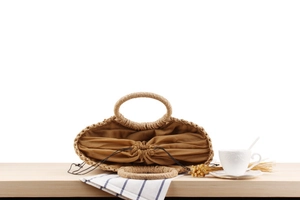 Close-up of woven straw handbag with ring handles and drawstring inner bag on wooden table