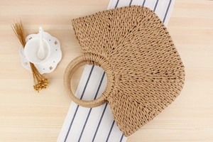 Macro view of woven straw fibers and semi-circular handle on minimalist beach handbag