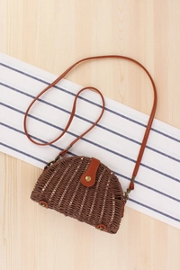 Detailed top view of a semi-circular straw woven bag with leather flap and metal feet