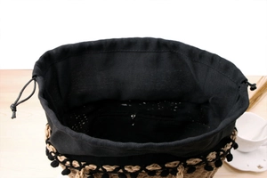 Detail view of woven paper rope beach bag with pom-poms and interior zipper pocket