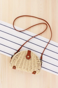 Detail of woven straw semicircle bag with brown leather clasp and slender shoulder strap
