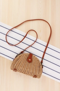 Detail of half-moon woven straw bag featuring brown leather strap and metal clasp closure