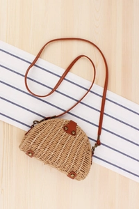 Detail view of woven semi-circle straw bag with brown leather strap and rivet accents