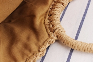 Detail of woven straw handle and durable linen lining of the small summer beach handbag