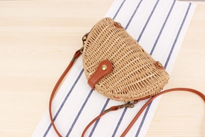 Detail of a semi-circular woven straw saddle bag with brown leather flap and metal clasp