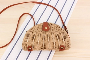 Detail of semi-circular woven straw bag with brown leather strap and gold metal clasp