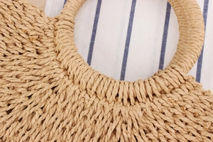 Close-up of a natural straw woven bag showing the round handle and textured craft details