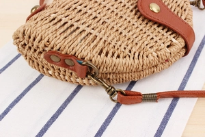 Detail of woven straw handbag featuring brown leather strap and bronze metal rivets