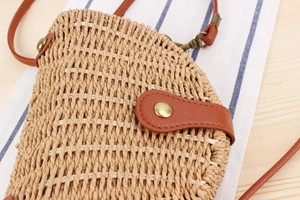 Detail of woven straw shoulder bag with brown leather trim and magnetic closure