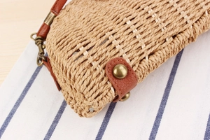 Detail view of woven straw bag bottom with brown leather reinforcement and metal studs