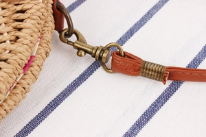Detailed macro view of woven straw bag featuring vintage bronze clasp and floral lining