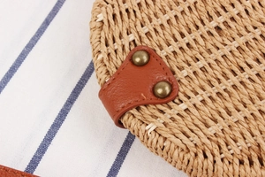 Detailed close-up of woven straw texture with brown leather trim and bronze rivets