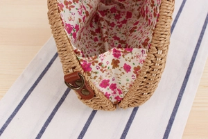 Detail of floral lining and leather strap hardware on a semi-circular straw bag