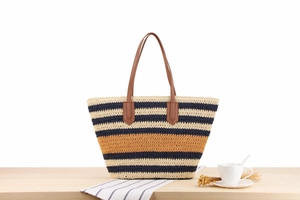 Detail of multi-color striped woven tote with brown leather handles on a wooden table