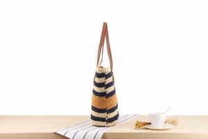 Detail of striped woven tote bag with brown leather straps on a wooden table setup