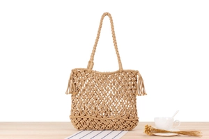 Detail of hand-woven macramé shoulder bag with long fringes on a wooden table