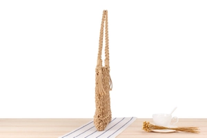 Detailed side view of beige woven cotton shoulder bag with decorative tassels and strap