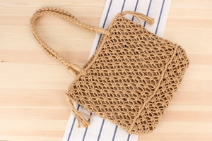 Detail of hand-woven cotton rope mesh tote bag with bohemian tassels on wooden table