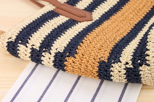 Detail of color-block striped woven bag with leather handle joints on wood background