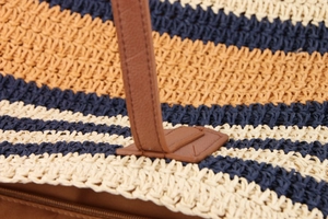 Close-up of multicolored straw woven bag with leather handles and navy blue stripes