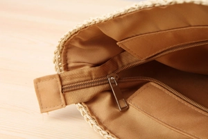 Detail view of the brown fabric lining and secure zipper pocket inside a woven straw bag