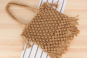 Detail of handmade woven cotton net tote bag with fringe tassels on a wooden surface