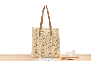 Close-up of beige woven paper rope tote bag with brown leather handles and zipper
