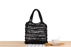 Detail shot of black woven cotton rope mesh bag with thick braided handles on wood surface