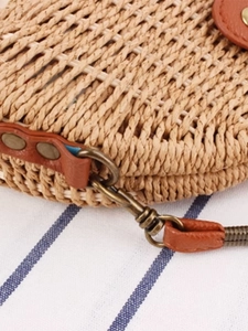 Detailed close-up of woven paper rope shoulder bag with brown leather strap and bronze hardware