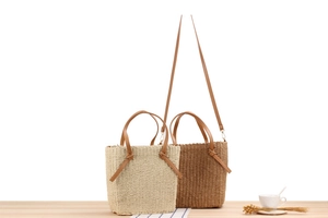 Detail of woven straw tote bags in beige and dark brown with synthetic leather straps