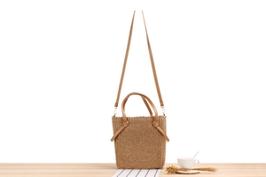 Detail of woven straw handbag featuring brown leather handles and adjustable shoulder strap