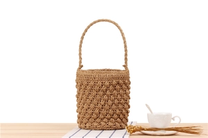 Detailed close-up of a handmade cylindrical straw bucket bag with woven ball texture