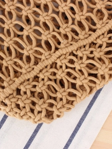 Handmade macrame woven shoulder bag in light brown on a striped fabric background