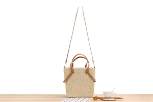Detail of hand-woven beige straw tote with brown leather handles and gold-tone hardware