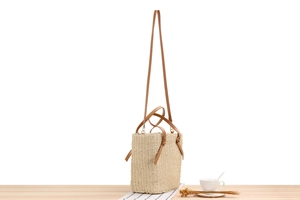 Detail of woven straw tote bag with brown leather handles on a minimal wooden table