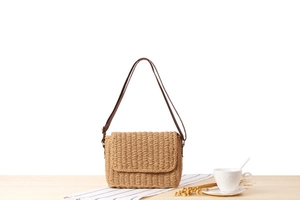 Detailed view of handmade woven straw bag featuring a brown leather strap on a wooden table