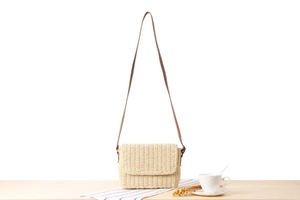Detail of hand-woven beige straw crossbody bag with brown strap and magnetic flap closure