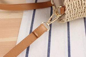 Detailed close-up of woven beige straw texture with brown faux leather strap and gold buckle