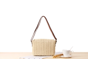 Close-up of cream woven crossbody bag with brown leather strap on a wooden table