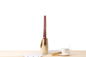 Detail view of handmade cream woven bag with dark brown leather strap on wooden surface