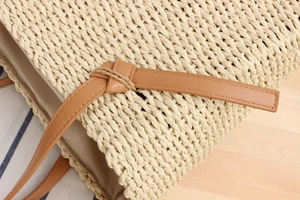 Detailed close-up of woven straw bag texture with brown leather knotted shoulder strap