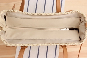 Detail view of woven straw tote bag with fabric lining and metal zipper closure