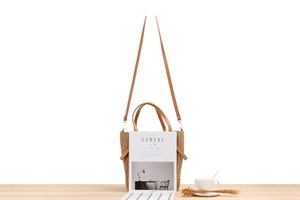 Detail of woven straw tote bag with brown leather handles and adjustable shoulder strap