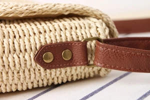 Detail of hand-woven straw bag showing brown leather strap and bronze rivets
