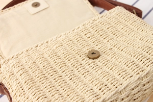 Detail of magnetic bronze clasp and fine texture on a hand-woven straw crossbody bag