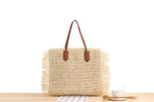 Detail view of woven paper rope tote bag with bohemian tassels and leather handles
