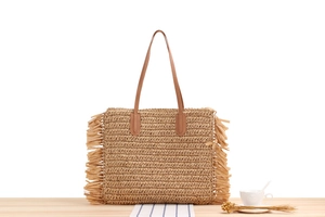Detail of woven straw tote bag featuring decorative side tassels and slim straps